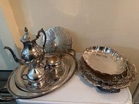 Full view of silver tea and coffee set with trays and trivet arranged on a table