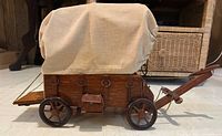 Side view of covered wagon lamp showing fabric canopy, wooden panel body, metal rings and chains, miniature toolbox, and wheels.