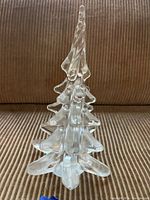 Front view of the clear glass Christmas tree on a ribbed brown fabric surface showing the layered branches and twisted top.