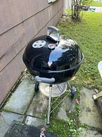 Full view of the black Weber charcoal grill with the lid on, showing the vent and temperature gauge on top, and handle on the lid and body.