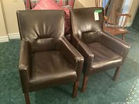 Two brown vinyl armchairs placed side by side. Both feature straight wooden legs and show damage to the seats.