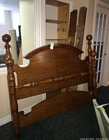 Photo of assembled wood headboard and footboard leaning against wall, showing carved wooden features and round finials on posts