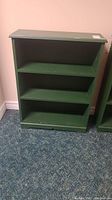 Front and side view of the green bookcase showing three shelves and general wear.