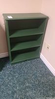 Front view of the small green wooden bookcase showing three shelves.