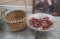 Woven basket next to a glass potpourri bowl on a metal stand filled with potpourri on a tiled floor.