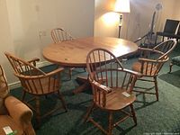 Four solid wood armchairs arranged around a round wooden table indoors, showing full set and design details.