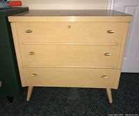 Front view of vintage cedar chest, beige with brass handles, showing three drawers with lock on the top drawer.