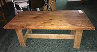 Front view of wood trestle style coffee table showing rectangular top with visible grain and surface marks, sturdy legs, and a horizontal support beam.