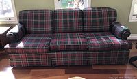 Frontal image of plaid fabric sofa showing three seat cushions and rolled armrests, capturing upholstery and condition details.