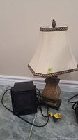 Photo show heater and lamp together, heater is black with mesh front and knobs, lamp has fabric shade with brown trim and decorative base.