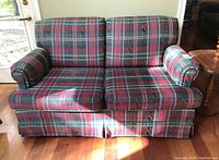 Front view of the plaid fabric upholstered loveseat showing two zippered, removable seat cushions and matching back cushions, set on a hardwood floor.