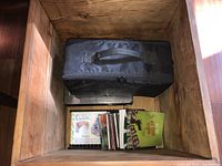 Wooden crate containing a black fabric carrying case with handle and some CDs next to it.