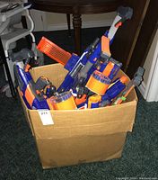Box containing multiple Nerf blasters and magazines in blue and orange color scheme.