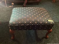 Full view of the top and side of the upholstered ottoman showing the floral textile pattern and wooden legs.