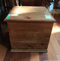 Side view of the pine storage box showing wood grain and hinged lid with rounded edges on wooden floor.