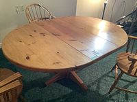 Top view of oval pine table with leaf inserted and two wooden chairs surrounding it on carpet floor.