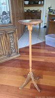 Full view of the wooden plant stand showing its round top and tripod base in a home setting.