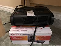 Photo of the Classic Turbo Heater & Fan unit sitting on its original box showing the front grille, control knobs and power cord.