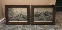 Two framed black and white Cole Bowman prints sitting on the floor against a wall, visible titles 'Harvest Time' and 'Summer Plowing', rustic wooden frames