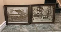 Photo showing both framed prints side by side on tiled floor, sepia tone rural scenes with horse-drawn carriages and snowy cabin.