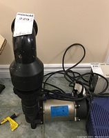 Front view of AquaScape pump with pipe and power cord on floor.