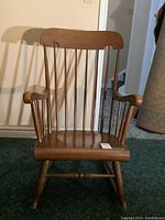 Front view of wooden rocking chair showing spindle back and armrests.