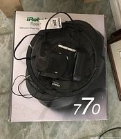 iRobot Roomba 770 vacuum robot with black docking station resting on original box, power cable visible.