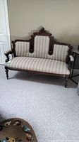 Full view of the vintage wooden frame settee with striped fabric upholstery on casters.