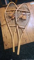 Full view of both wooden snowshoes laid flat on a wooden table showing the overall size and shape.