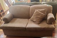 Front view of brown ultrasuede two-seater sofa bed with two cylindrical armrest pillows and one square throw pillow, showing overall structure.