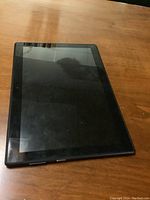 Front view of black Lenovo tablet with screen off, laying on wooden surface.
