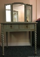 Full frontal view of the vanity table with tri-fold mirror showing twisted front legs and the two drawers with ring pulls.