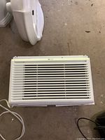 Front view of white window air conditioner unit with horizontal slats covering the vents.