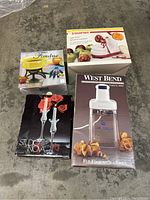 Photo of four boxed kitchen items: Apple peeler by Starfrit, yellow fondue set, West Bend electric curly cutter, Studio Nova candlesticks