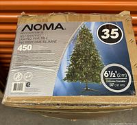Box of NOMA indoor self-shaping lighted pine tree, displaying product details including 450 pre-strung clear mini-lights, 2m height, and 1.27m diameter.