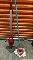 Photo showing a red Dirt Devil upright vacuum and a red triangle mop with a blue handle and white strands side by side.