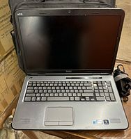 Front view of Dell XPS laptop showing keyboard, touchpad, and screen bezel with branding. Laptop surface worn and dirty, screen off.