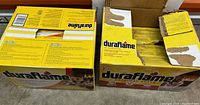 Two yellow Duraflame boxes side by side on the floor. One box is mostly sealed and the other is opened showing partial fire logs inside.