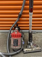 Dyson Animal DC32 vacuum cleaner showing hose, ball base, red cyclone unit, extension wand, and vacuum head with brushes and wheels. Unit appears dusty and used.