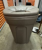 Front view of a large gray Rubbermaid garbage can with lid in a storage unit.