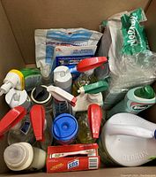 Photo showing assorted household cleaning products including spray bottles, detergent containers, cleaning pads, and plastic bags