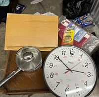 Photo showing a round Bates clock, a light wooden cookbook holder, and a stainless steel pot with glass lid.