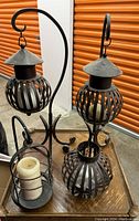 Photo showing 4 assorted black iron candleholders including two hanging spherical lanterns, one with visible candle inside, one small round holder with pillar candle