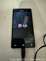 Front view of the LG smartphone powered on displaying the LG logo, connected to charger cable.