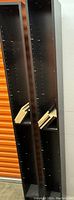 Two tall black media shelves, standing side by side, with multiple peg holes for shelf adjustment and some loose wooden slats inside.