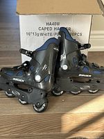 Side view of Bauer inline rollerblades showing black hard plastic shell with blue fabric inserts, straps, and wheels on frame