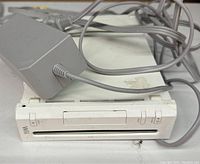 Close-up image of white Nintendo Wii console with power adapter lying on top, both showing signs of dirt and needing cleaning.