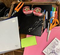 Photo showing assorted office supplies including scissors, tape dispensers, pens, markers, notebooks, sticky notes, folders, and paper.