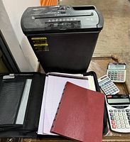 Lot contents including shredder, calculators, writing pad, binder, and organizer seen from higher angle.