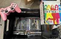 Black crate holding pink controller on left and rows of PS3 game cases with colorful spines; Disney Sing It box on right